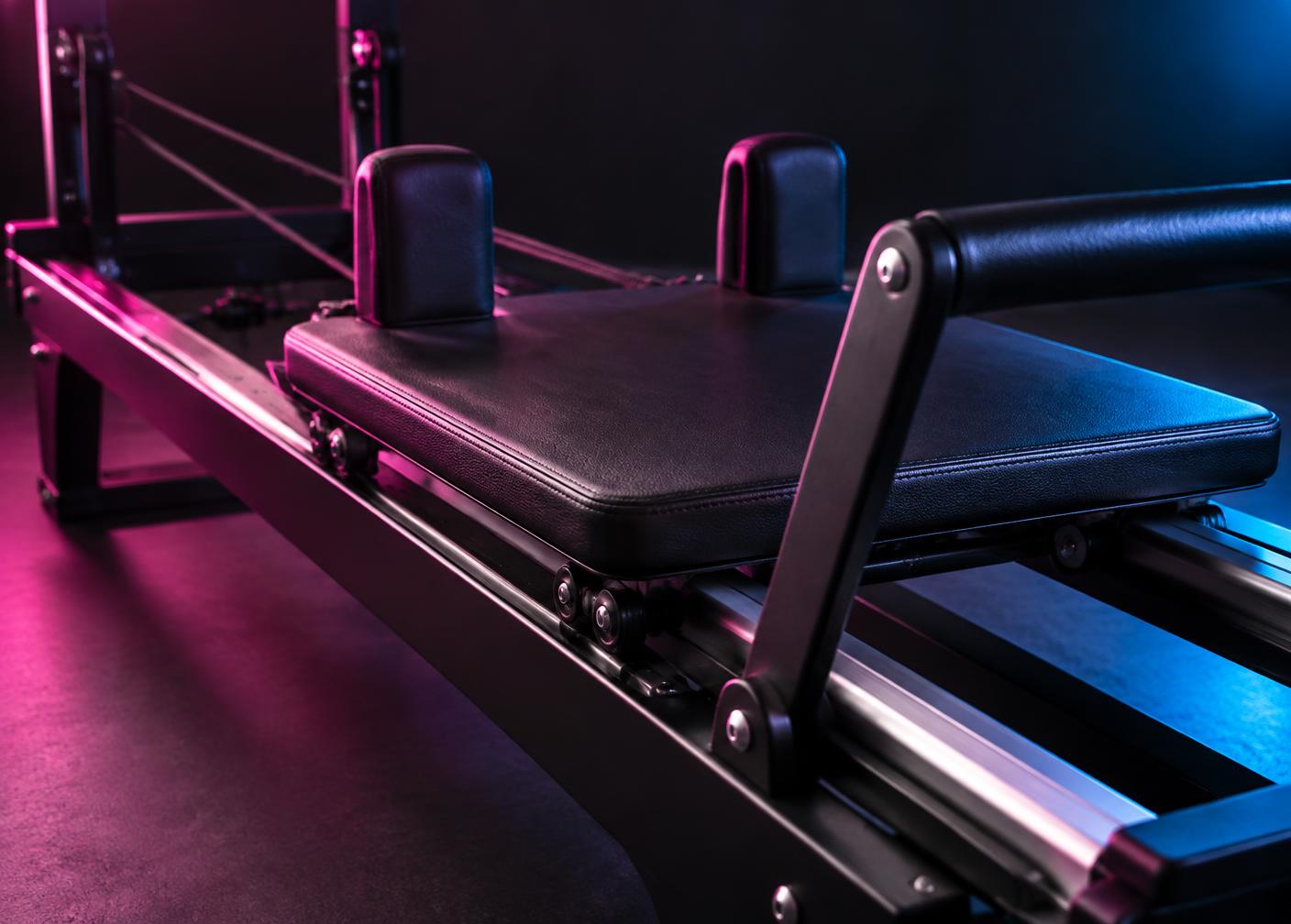 Close-up of a machine carriage, padded platform and black handles in magenta and blue light