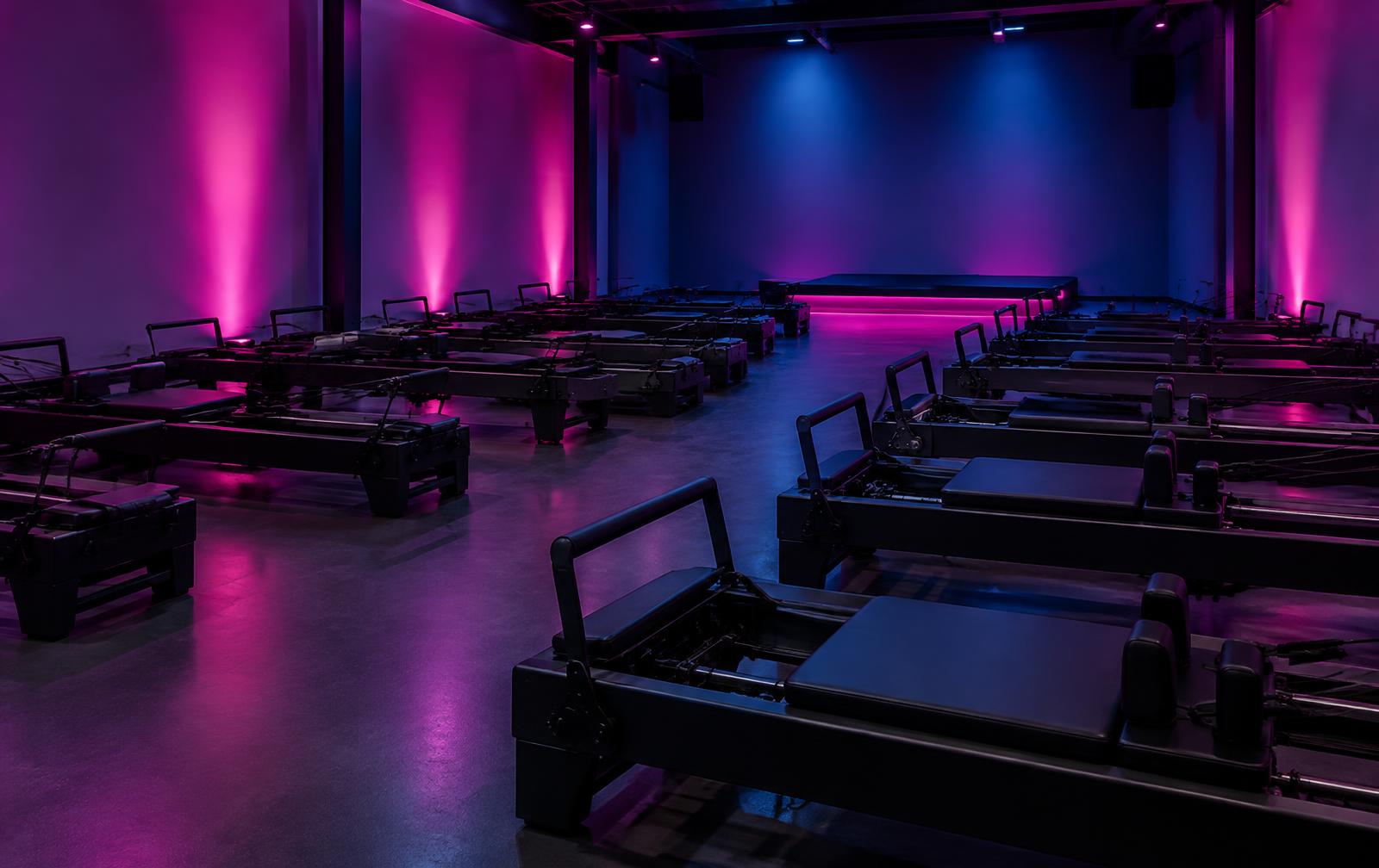 Dark studio with rows of training machines under magenta and blue chromotherapy lighting
